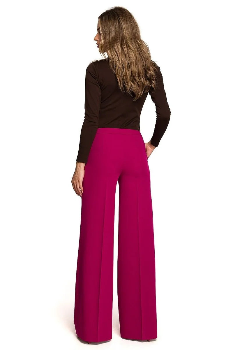 Woman from behind in a brown long-sleeve top and high-waisted bright pink palazzo pants.