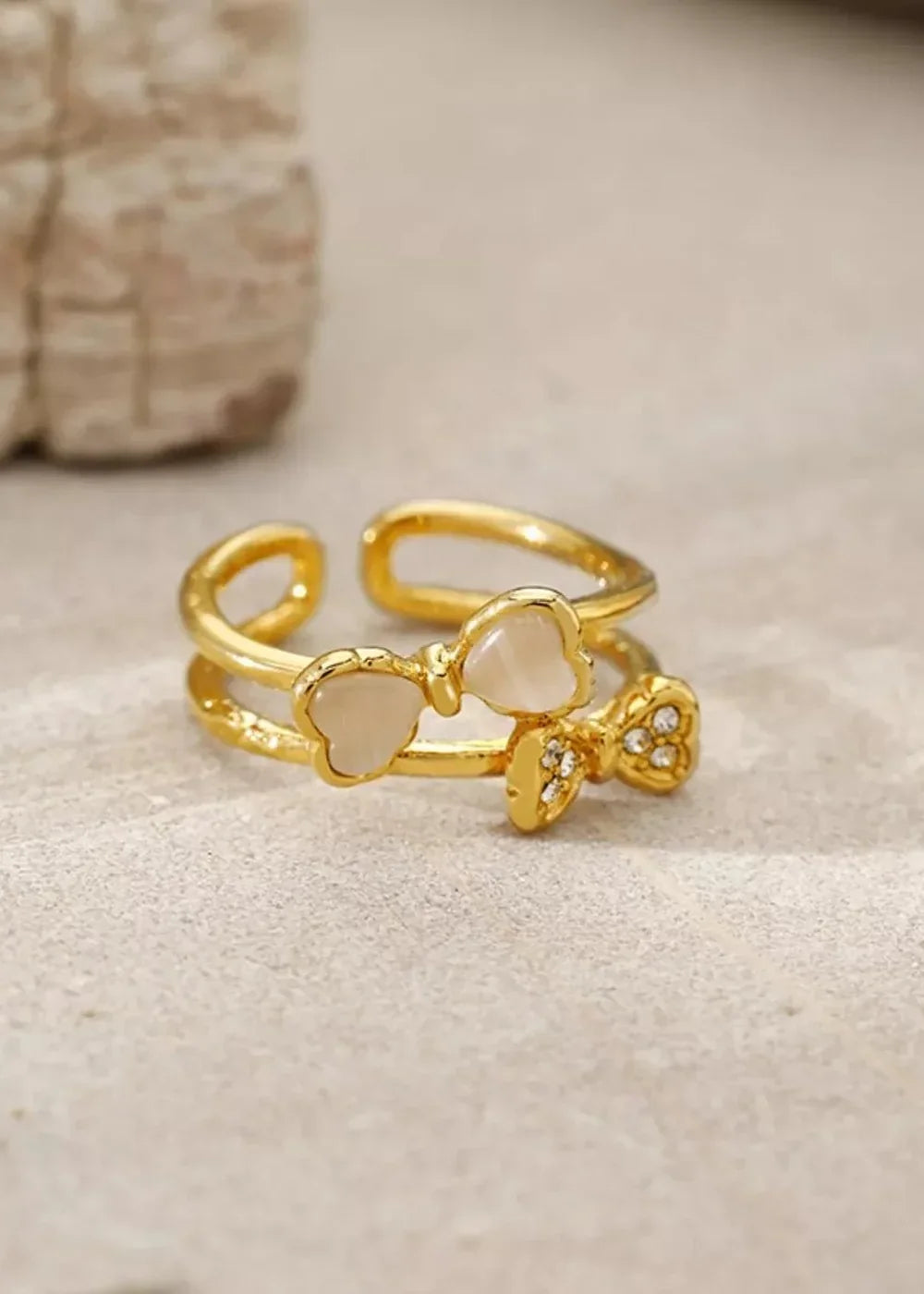 Gold double band ring with two bow charms, one with white resin and the other with rhinestones.