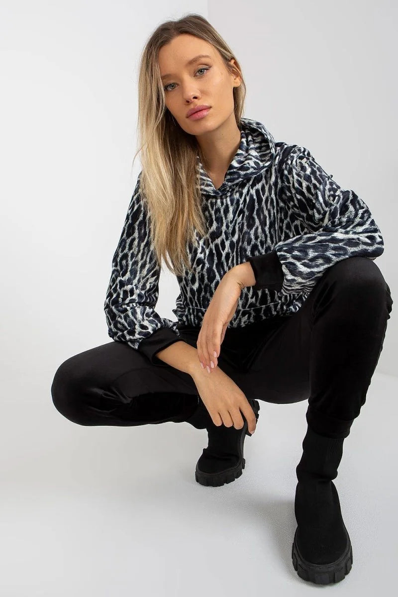 Woman in a black and white leopard print hoodie and black velvet pants, crouching.