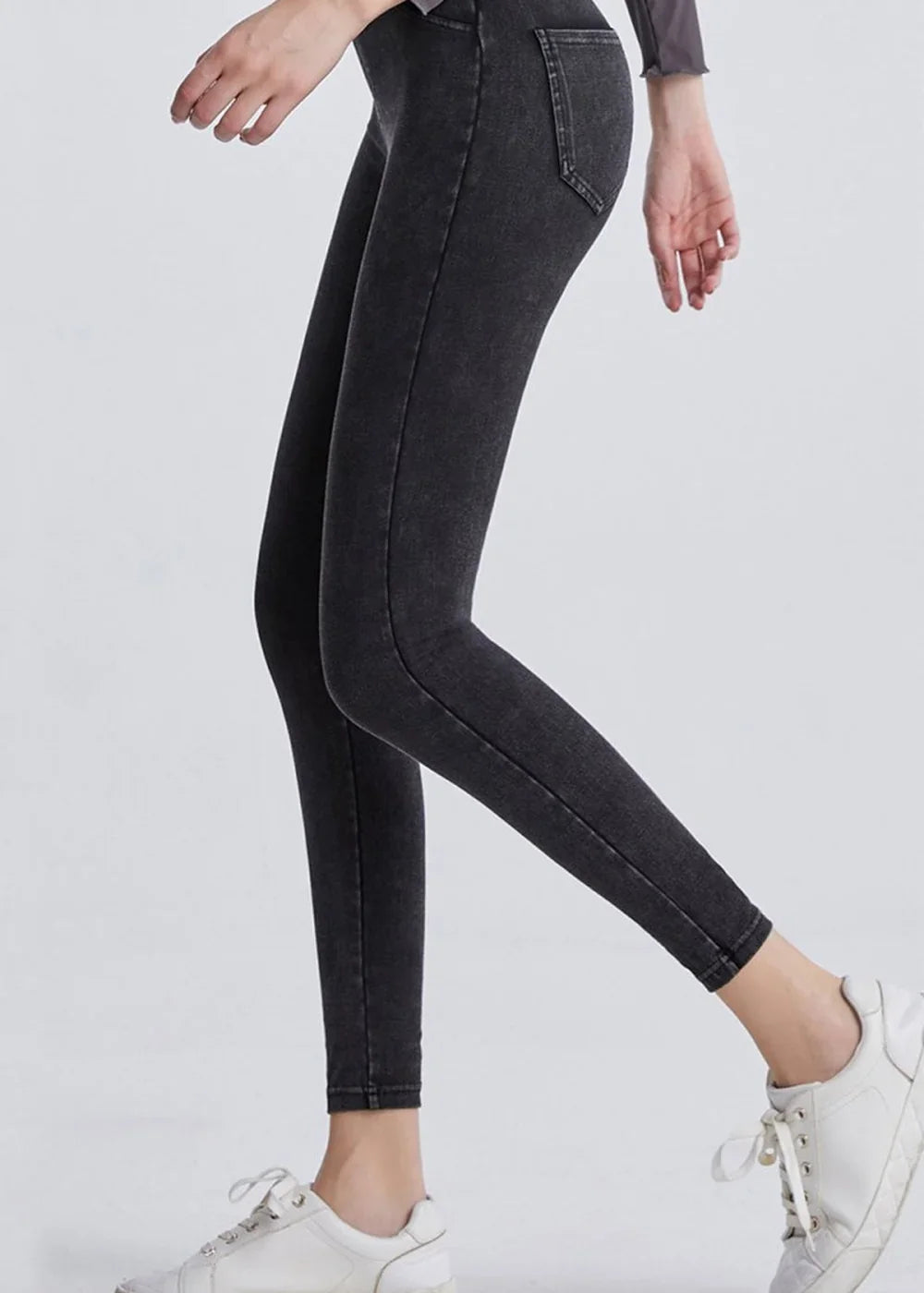 Close-up of dark wash denim-look leggings with a distressed texture, shown on a model wearing white sneakers.