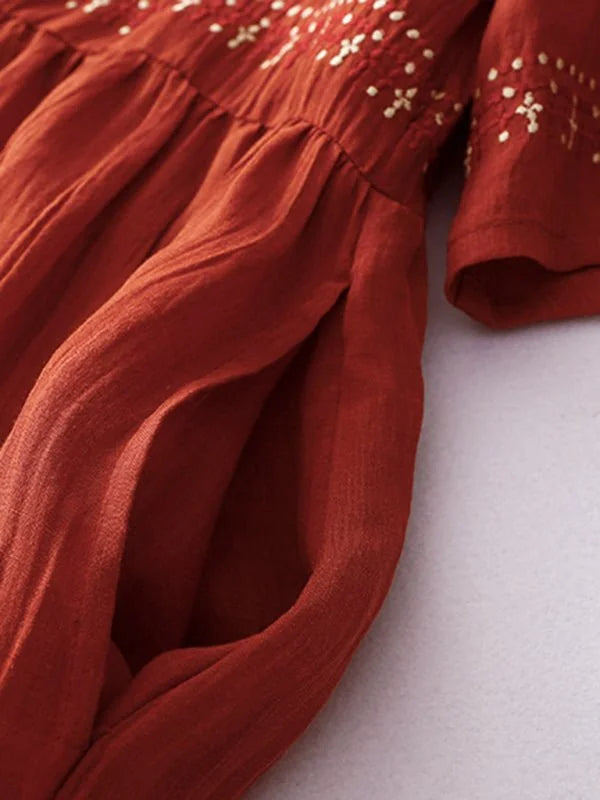 Close-up of a rust-colored linen-blend dress with white embroidery and deep pockets.