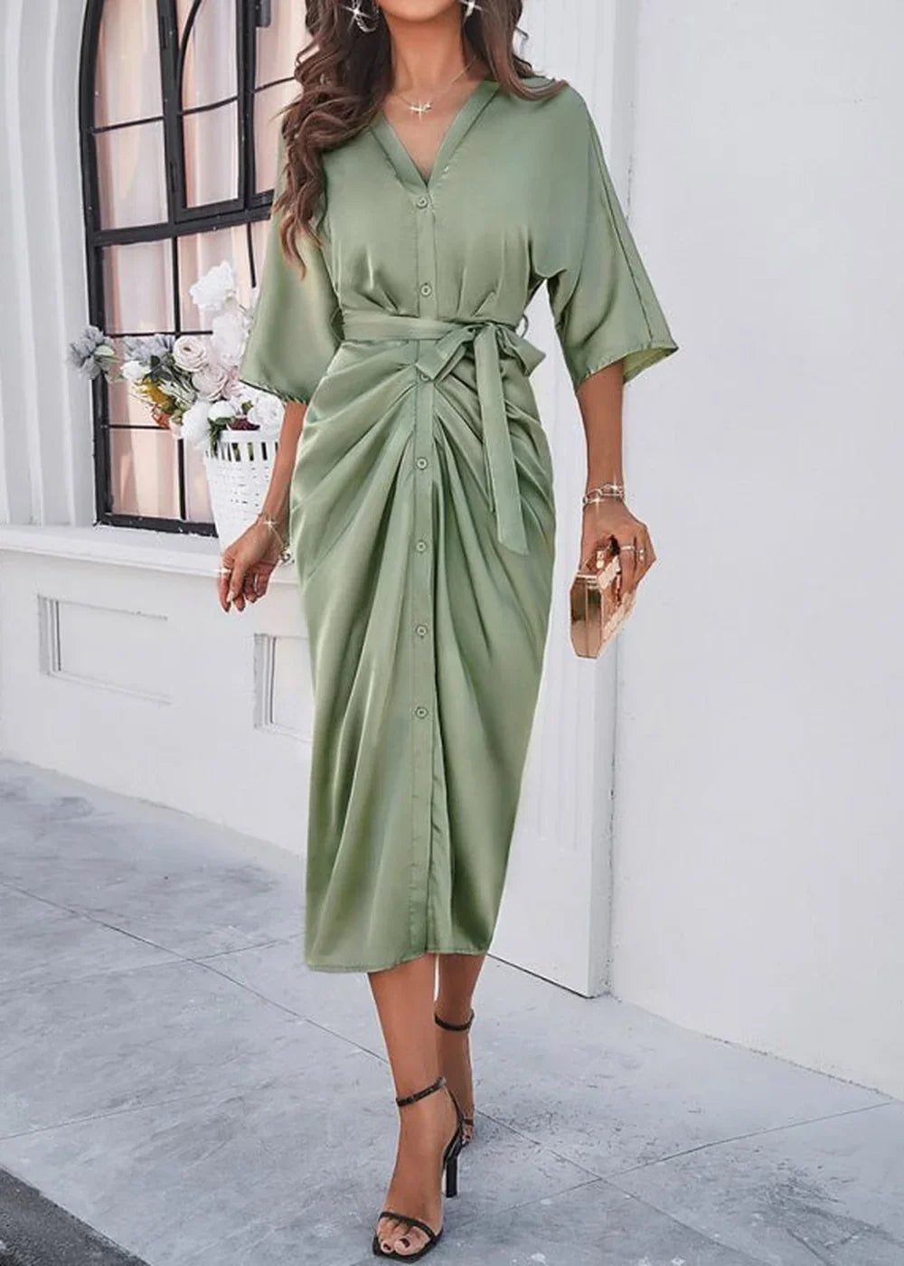 Sage green satin midi dress with a tie waist, V-neck, and button front detail, worn by a model.