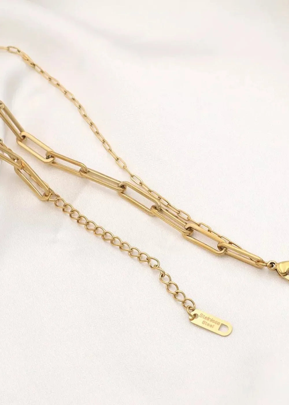 Close-up of a gold-plated stainless steel layered chain necklace with paperclip links and an extender chain.