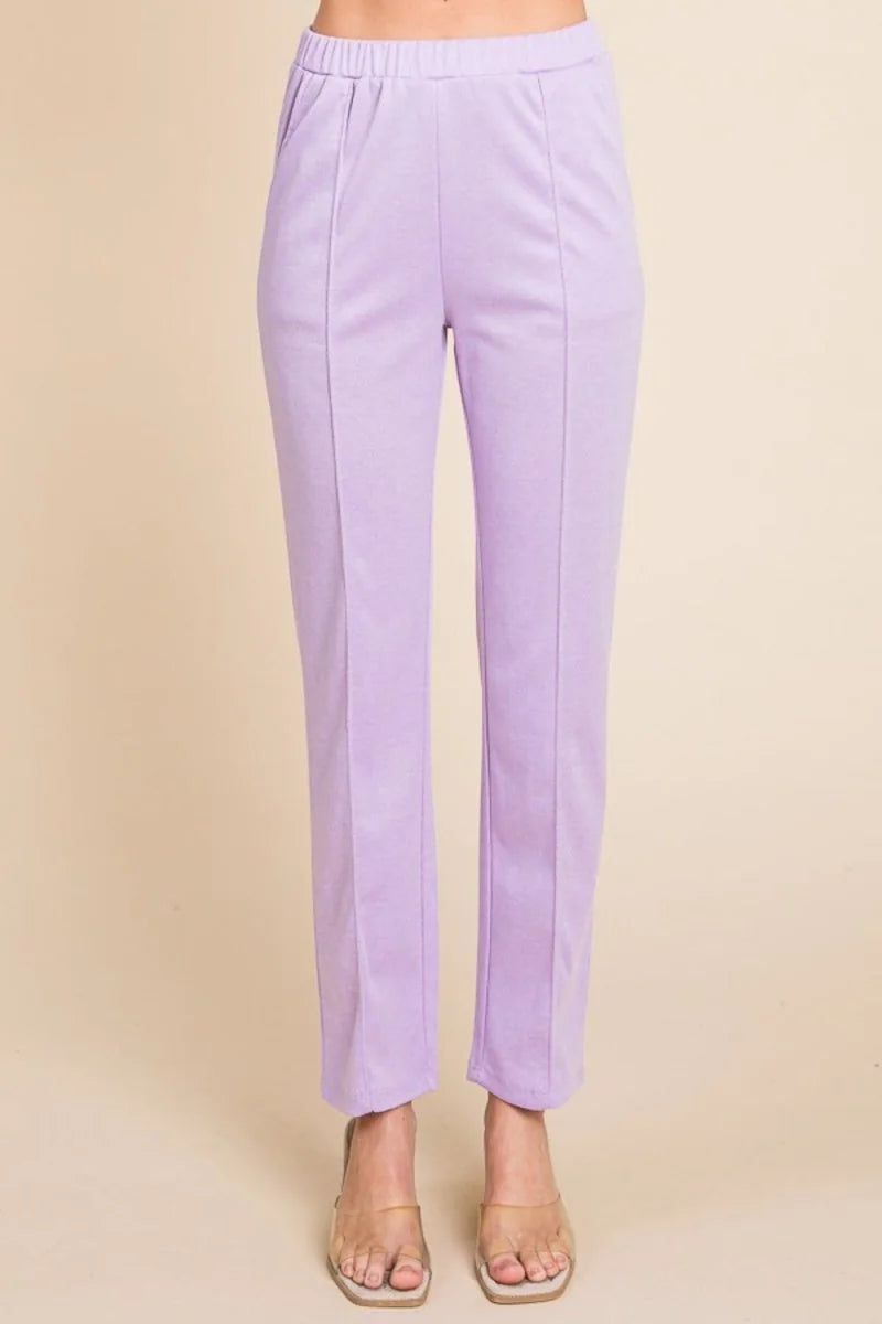 Lilac slim-fit pants with a smooth texture and front seam detail, worn with clear slide sandals.