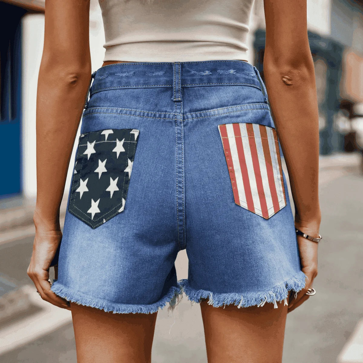 Blue denim shorts with frayed hem and American flag pocket details.