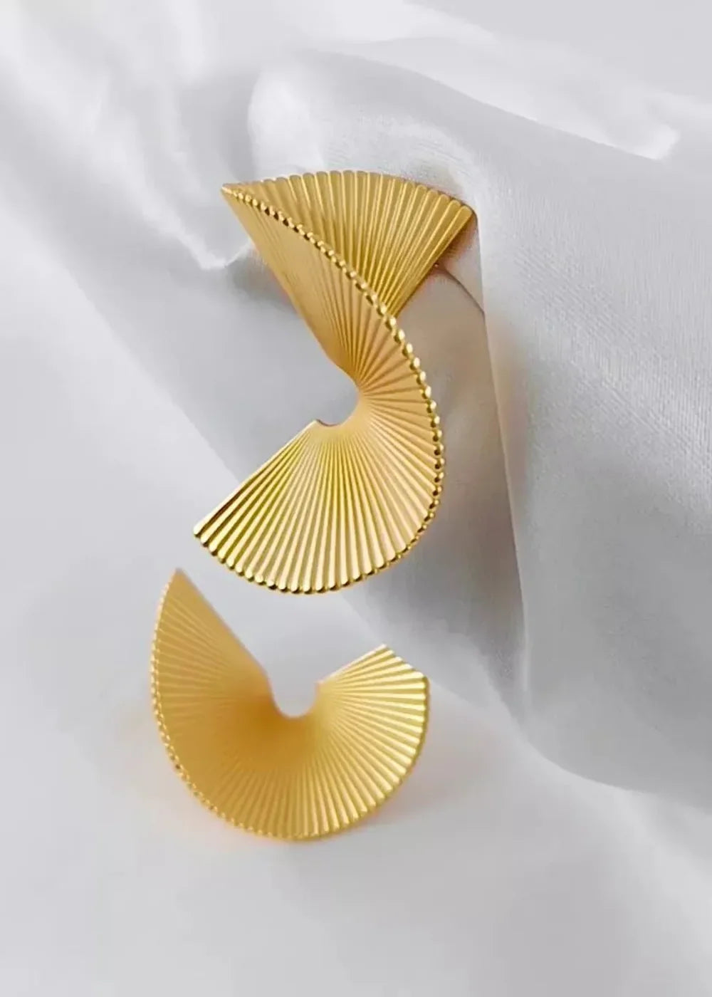 Gold-plated fan-shaped earrings with ribbed texture and beaded edges on white silk.