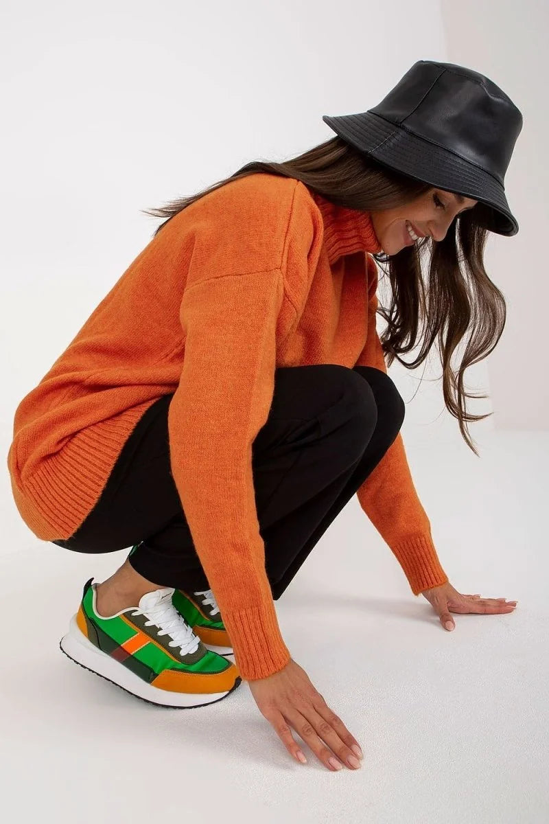 Woman in orange turtleneck sweater and black pants, wearing a black bucket hat and colorful sneakers.