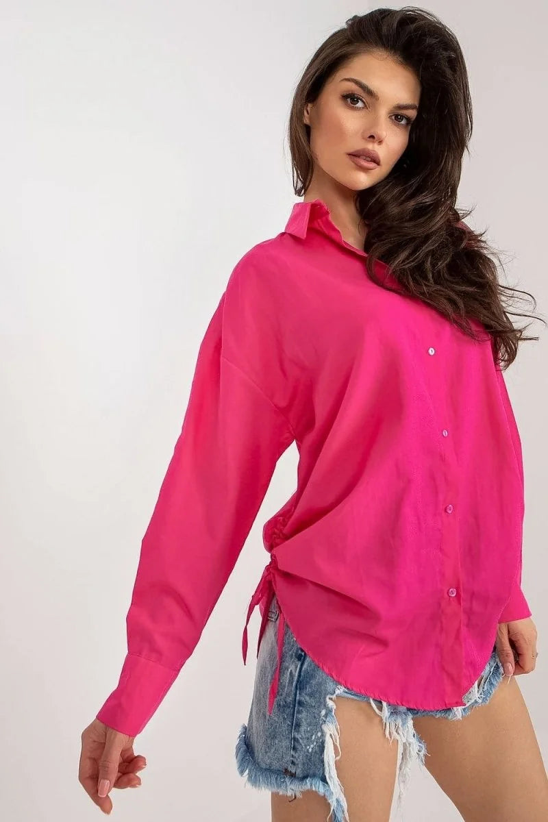 Fuchsia oversized button-down shirt with drawstring detail on sides, worn with distressed denim shorts.