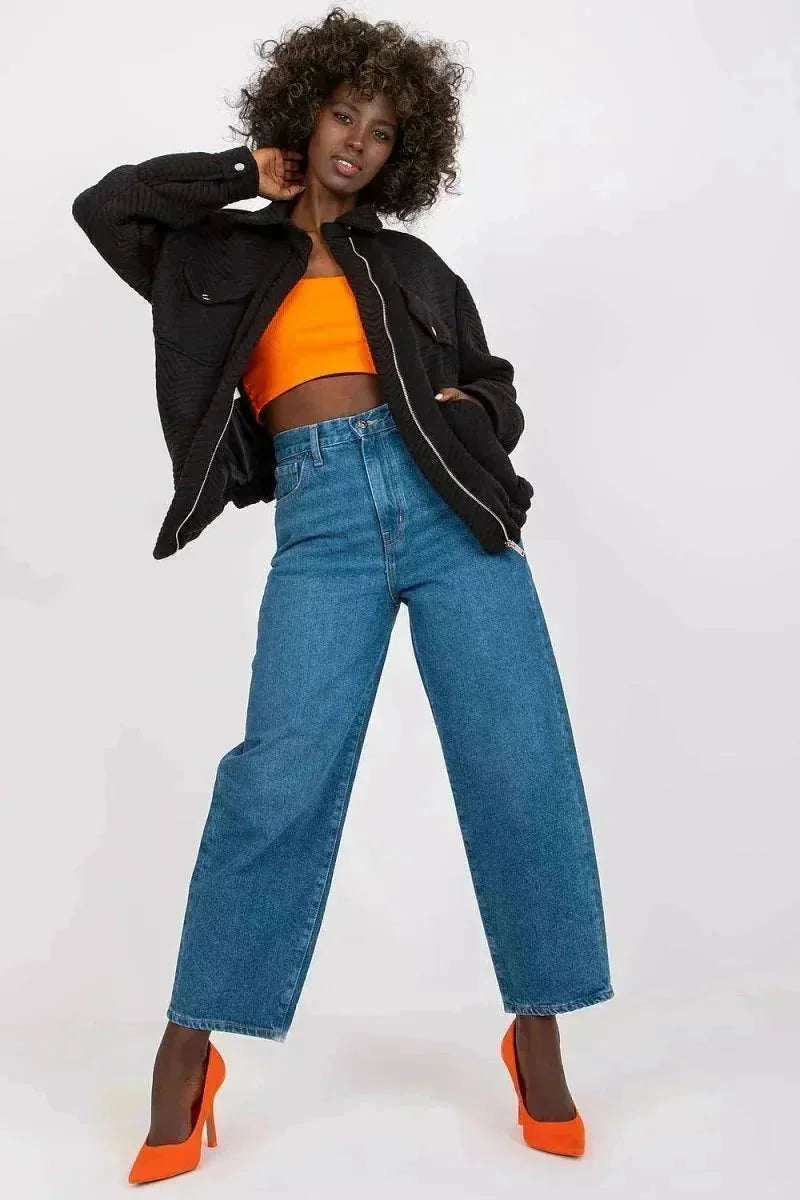 Black quilted jacket with a zip-up front, worn over an orange crop top with wide-leg denim jeans.