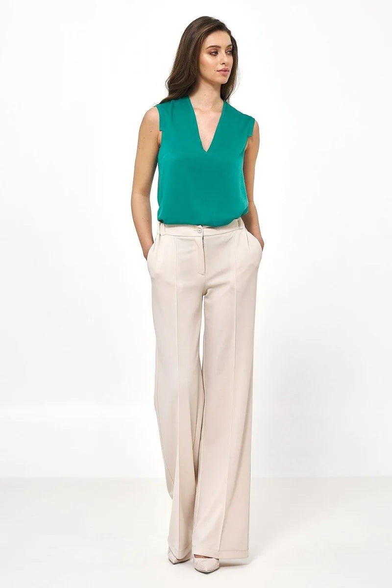 Full-length shot of a woman wearing relaxed-fit, cream-colored wide-leg trousers with a smooth texture and front pleats.