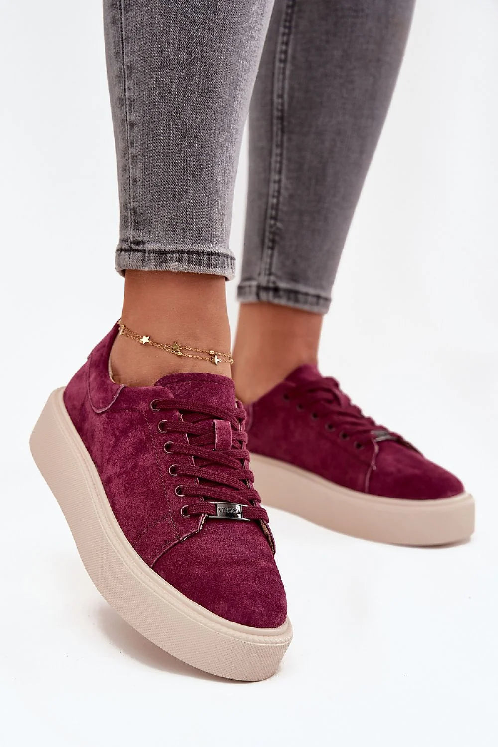 Close-up of plush burgundy suede sneakers with a thick cream sole and star anklet.