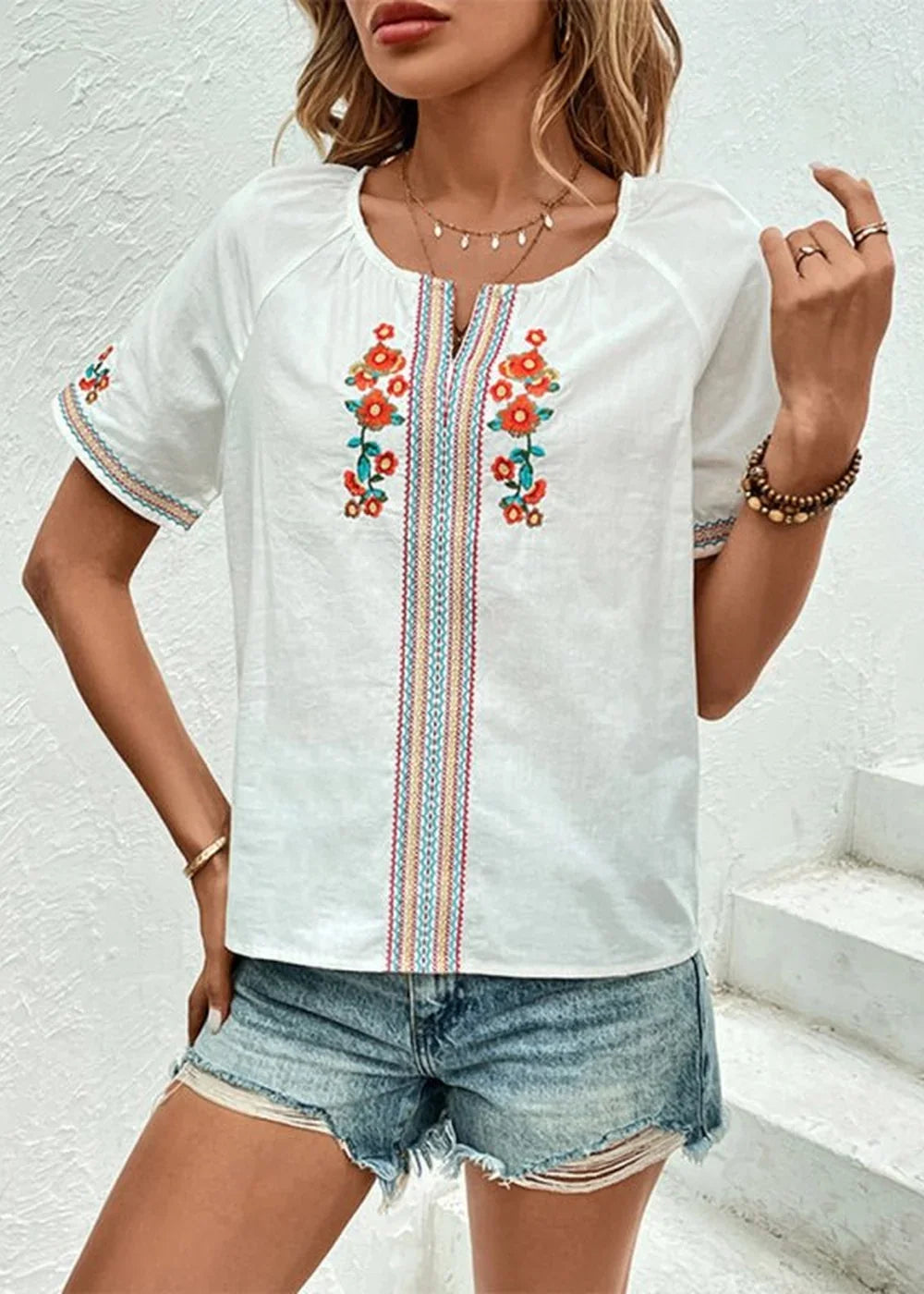 White embroidered top with floral detail and blue denim shorts on a model.