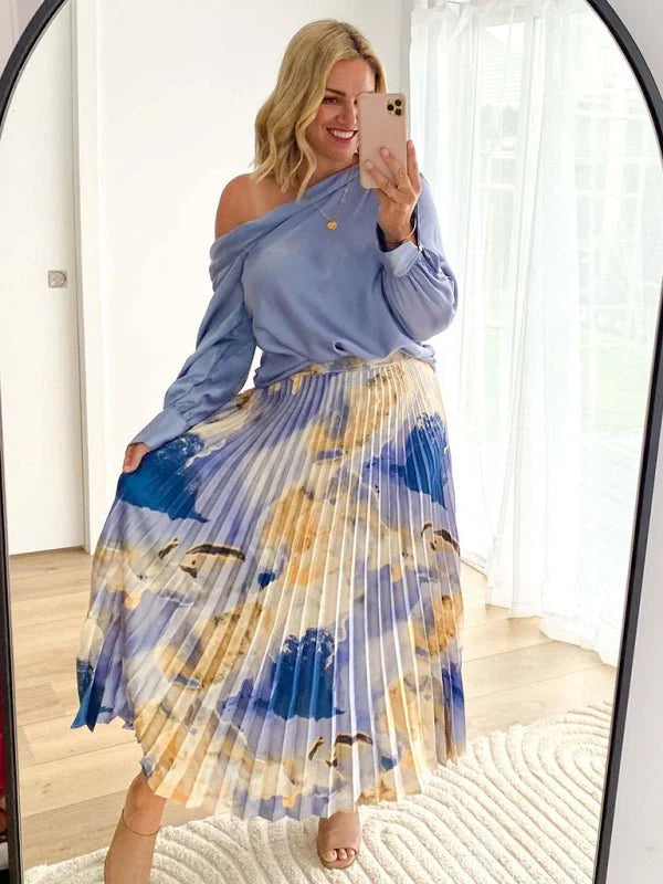 A flowing, pleated midi skirt with a watercolor print of blue, white, and tan abstract shapes.
