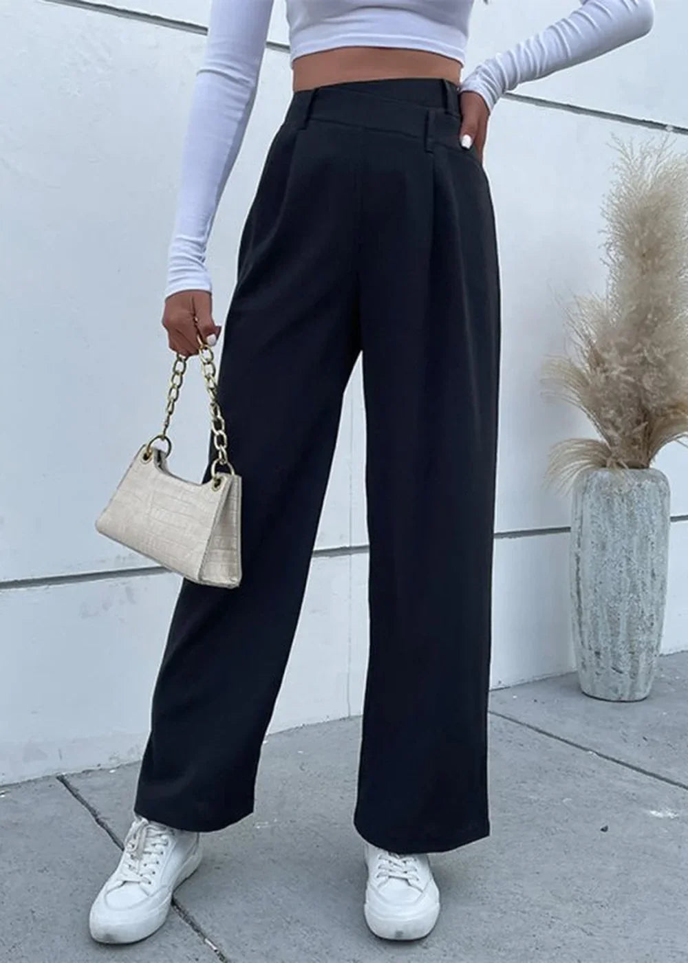 Black wide-leg trousers with a high waist and pleats, paired with white sneakers.