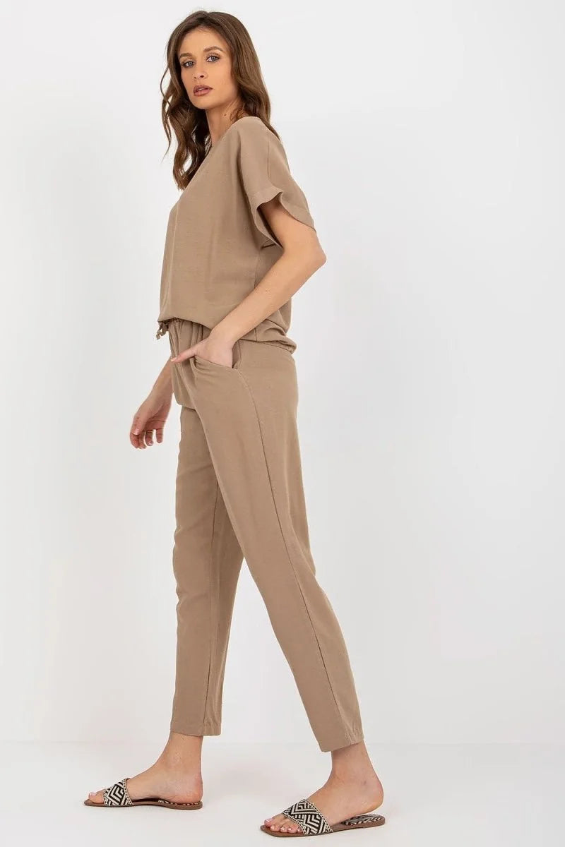 Woman in a taupe jumpsuit with short sleeves and pockets, wearing patterned sandals.