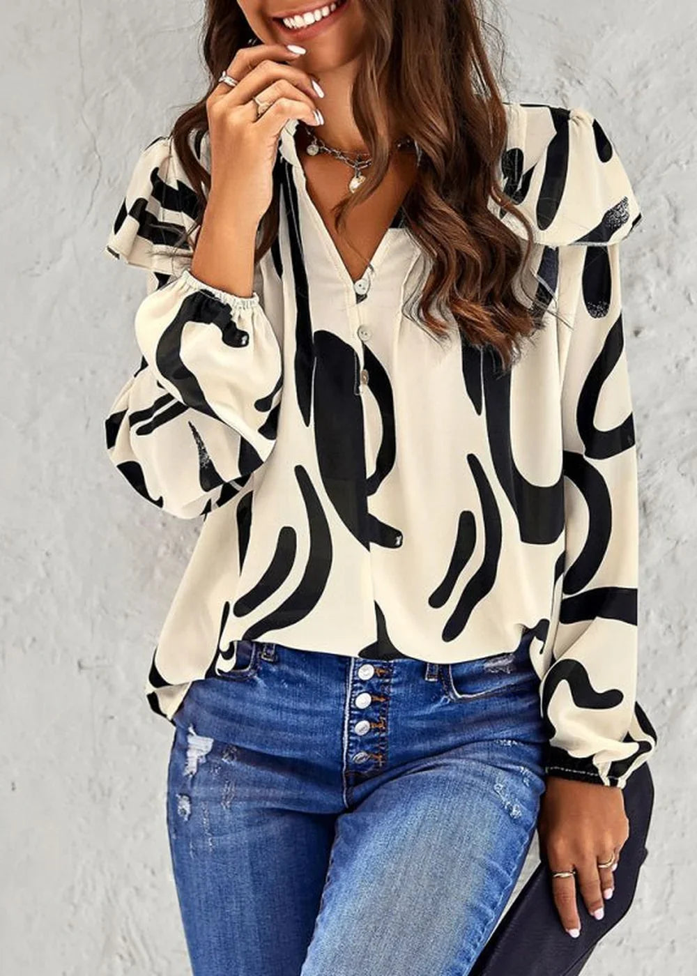 Cream blouse with black abstract print, ruffled neckline, and button details, paired with distressed blue denim.