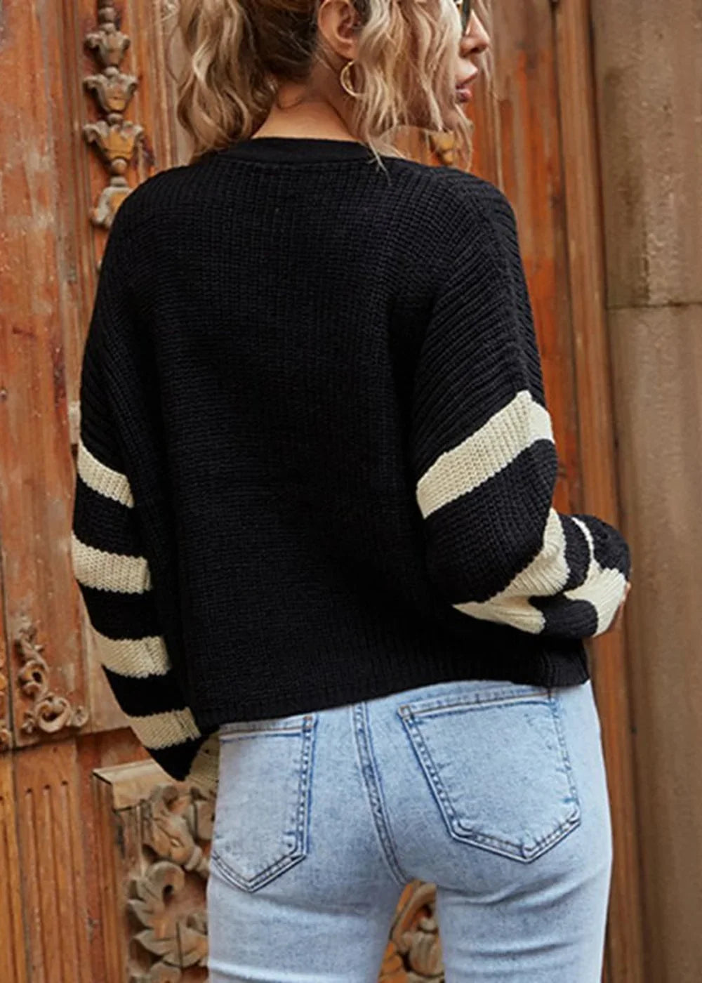 Black sweater with cream stripes on sleeves, paired with light wash denim jeans.