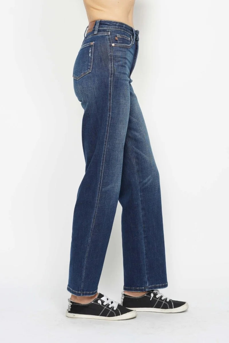 Dark wash, wide-leg jeans with a regular fit and white stitching, worn with black sneakers.