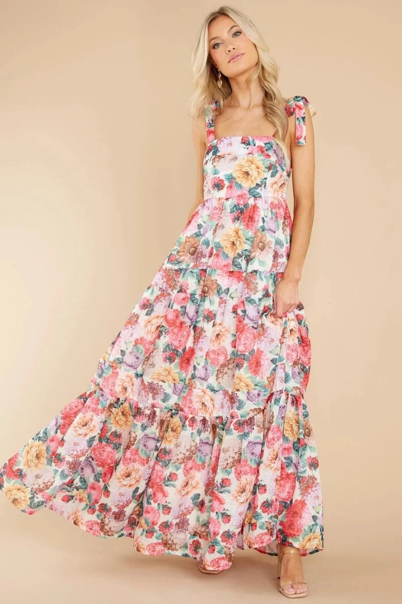 A woman in a flowing floral maxi dress with tiered ruffles and tie straps.