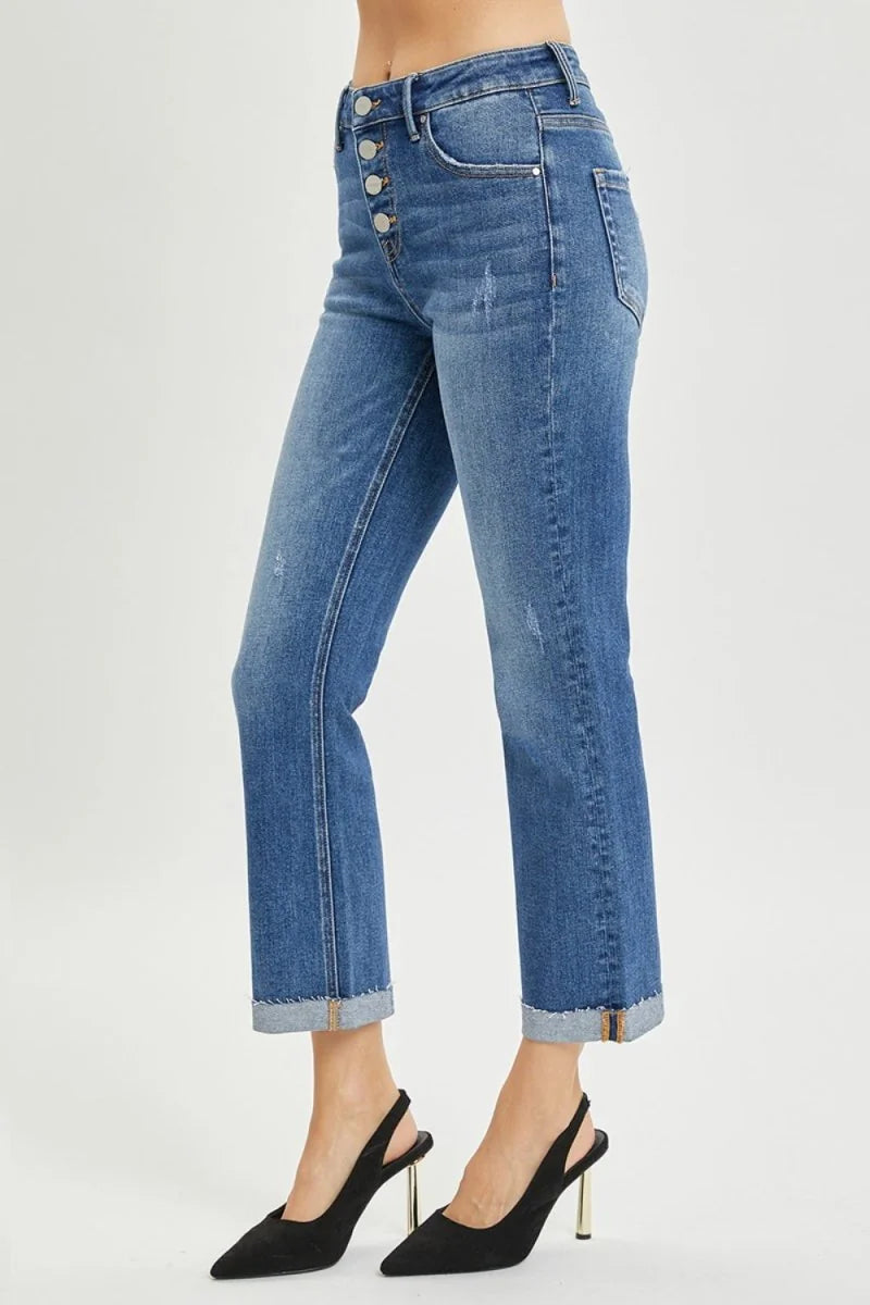 Distressed medium wash denim jeans with button fly, cuffed hem, and gold-heeled black slingbacks.