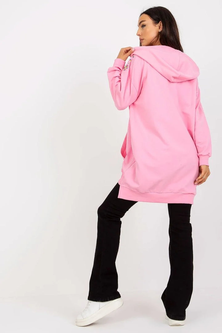 Pink oversized hoodie with embroidered details on sleeve, paired with black flared jeans.