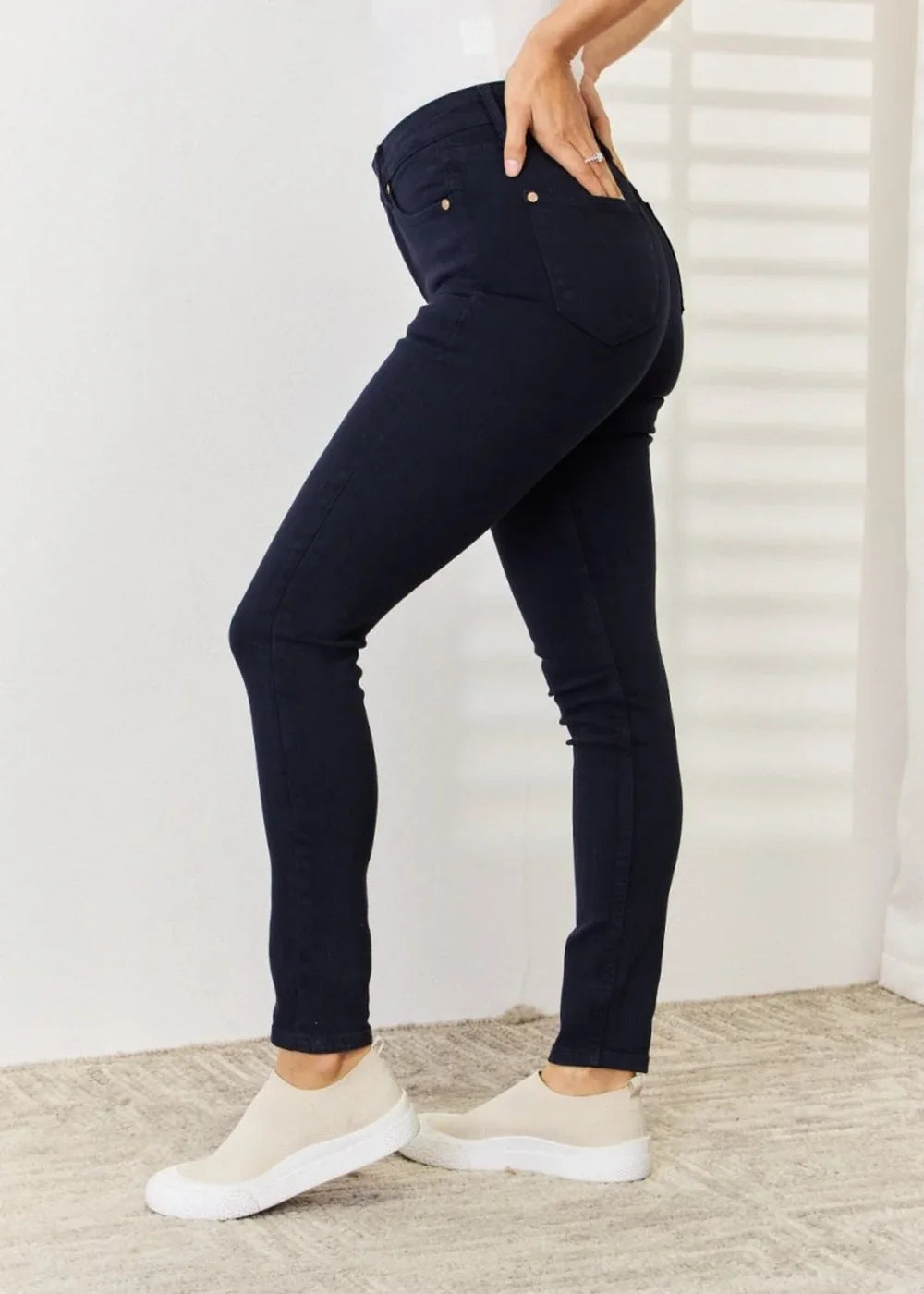 Navy blue skinny jeans with gold button details, worn by a model with cream slip-on sneakers.