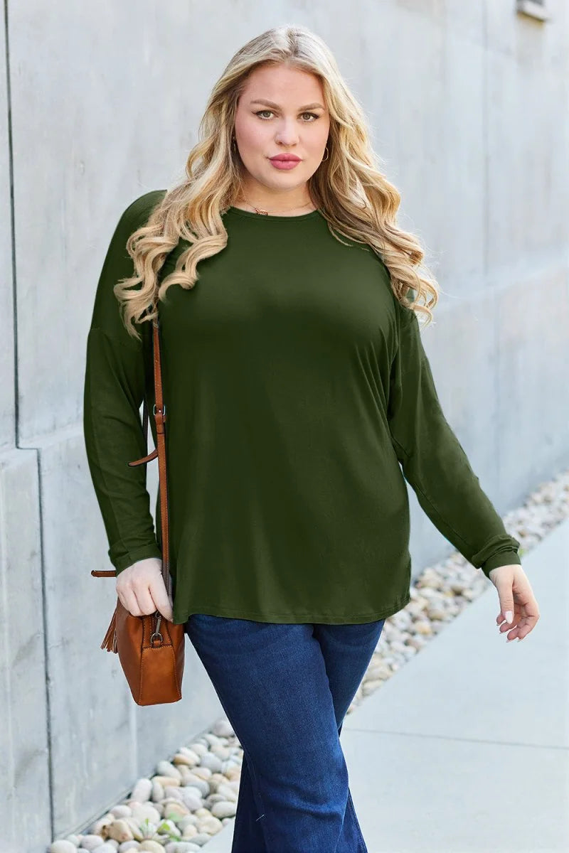 Woman with blonde wavy hair wearing a long-sleeved olive green top and dark wash jeans, holding a brown crossbody purse.