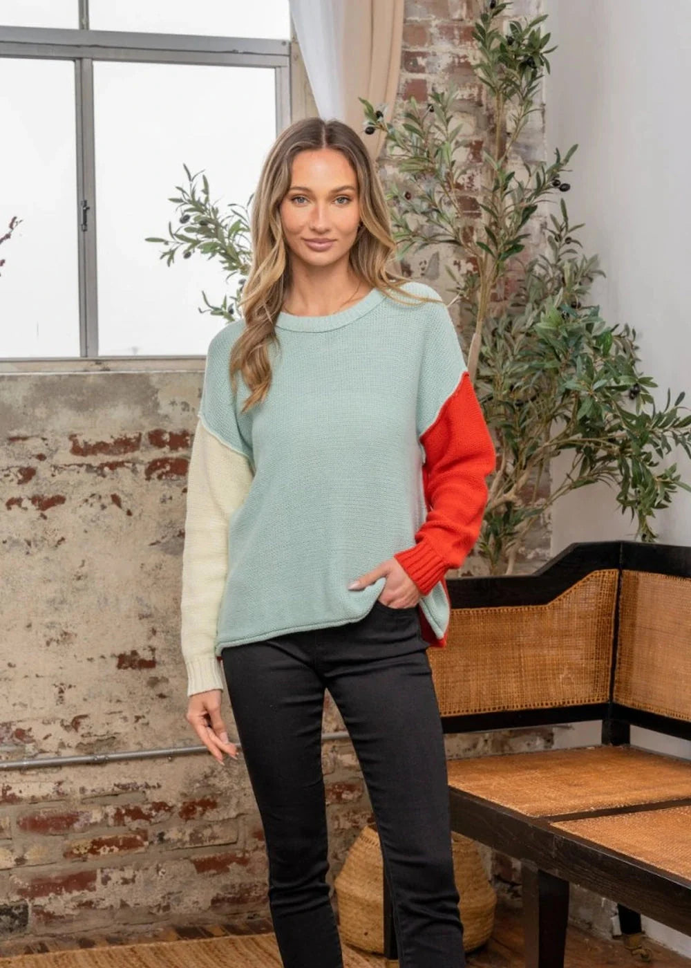 Light blue, cream, and red colorblock relaxed fit sweater on a woman with black jeans.