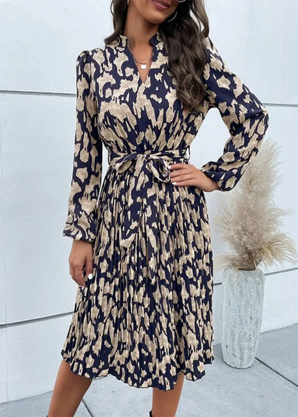 Woman in a long-sleeved, navy blue and tan abstract print midi dress with a tie waist and pleated skirt.