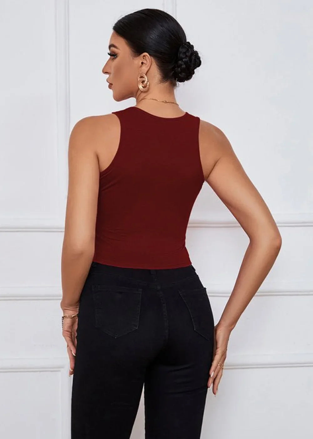 Back view of a woman wearing a burgundy sleeveless crop top and black skinny jeans.