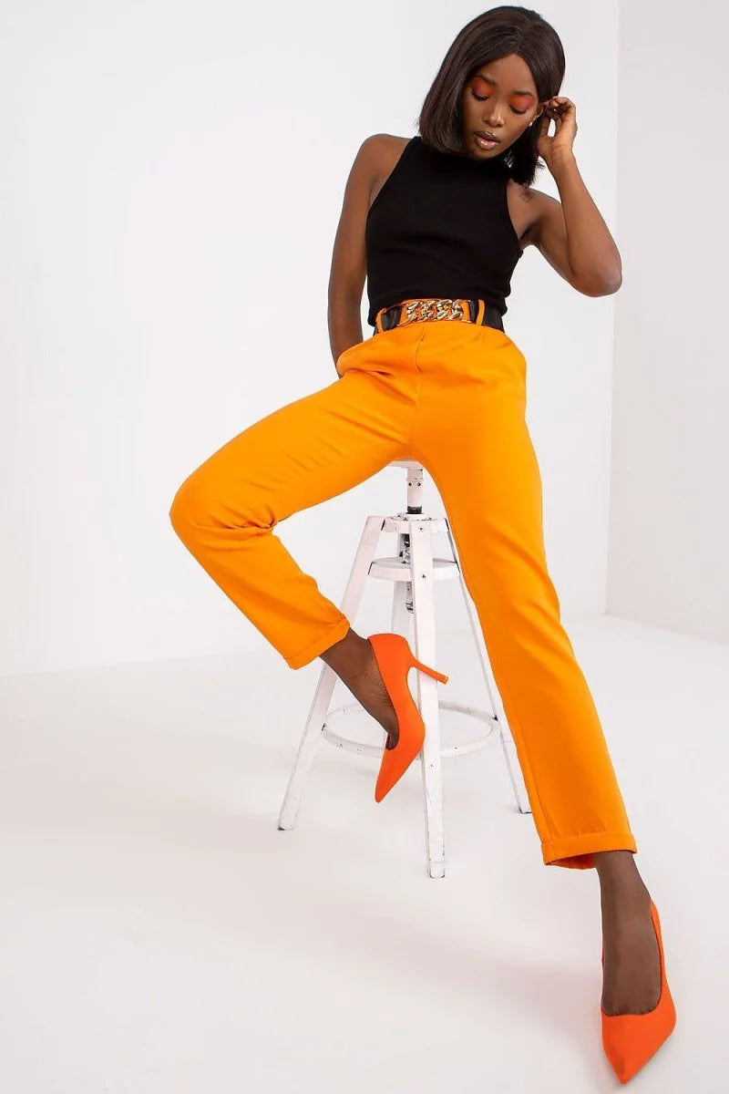 Model in bright orange, regular fit, straight-leg pants with a gold chain belt.