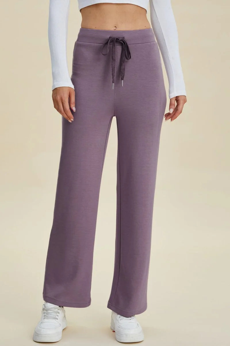 Dusty purple wide-leg sweatpants with drawstring waist and white sneakers on model.