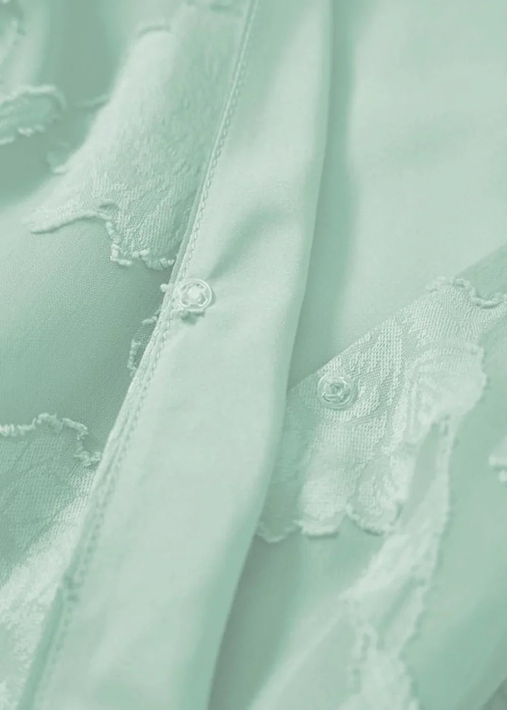 Close-up of a mint green dress with floral lace trim and pearl buttons.