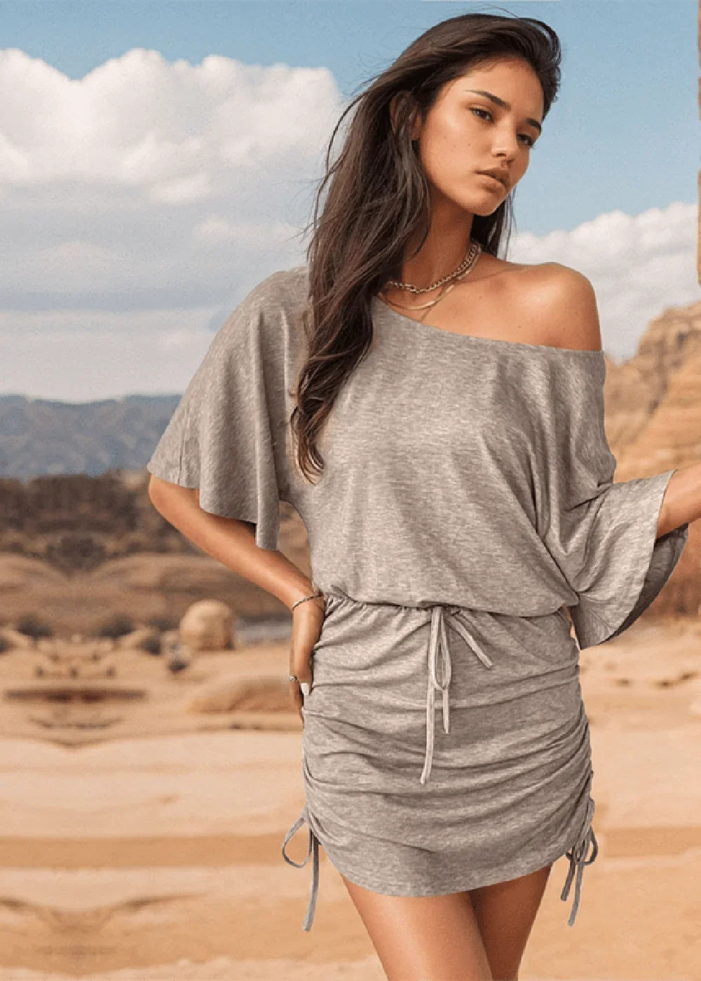 Grey off-the-shoulder ruched mini dress with drawstring waist and flutter sleeves, on model in desert landscape.