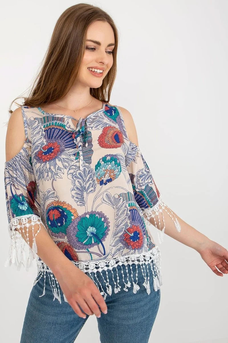 Beige cold-shoulder top with colorful floral print and white fringe trim.