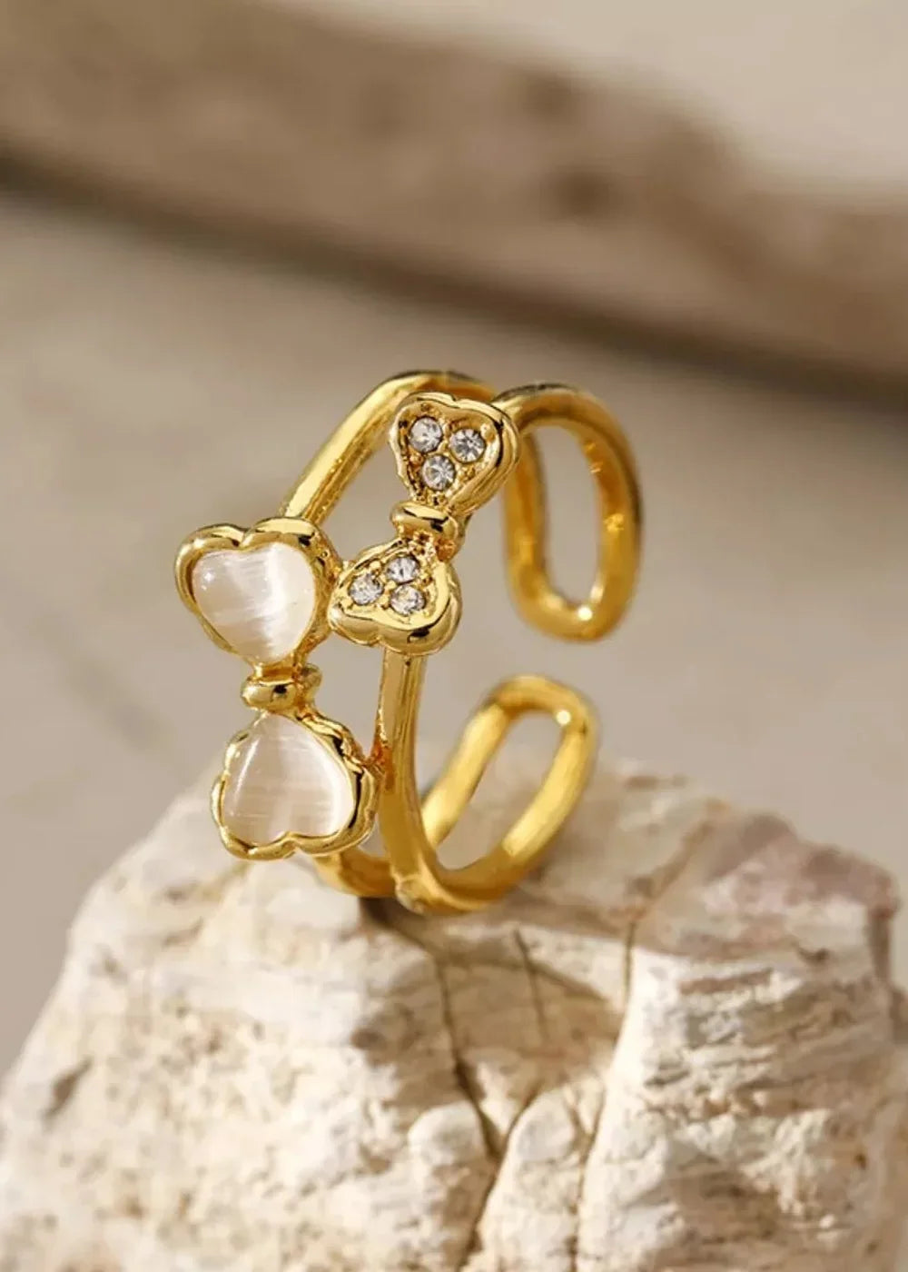 Gold adjustable ring with two heart-shaped white stones and rhinestone accents.
