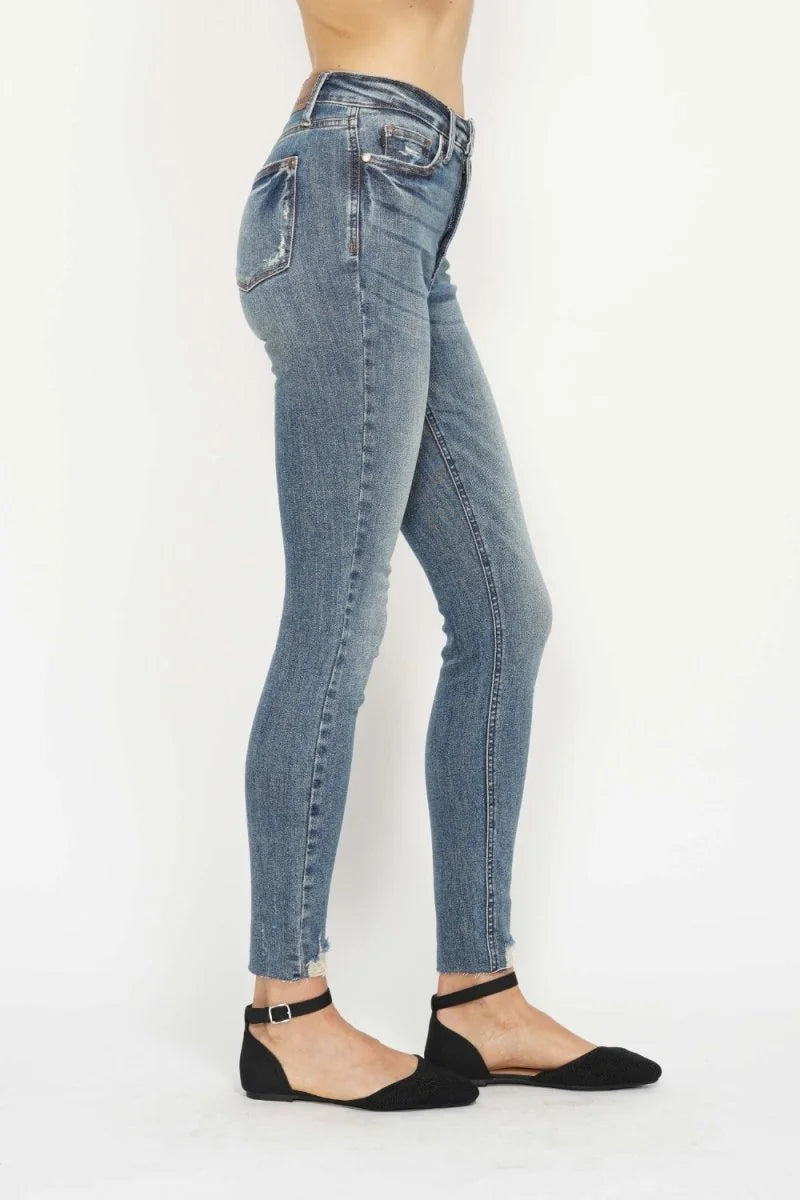 Side view of a model wearing medium wash distressed denim jeans with a frayed hem and black ankle strap flats.