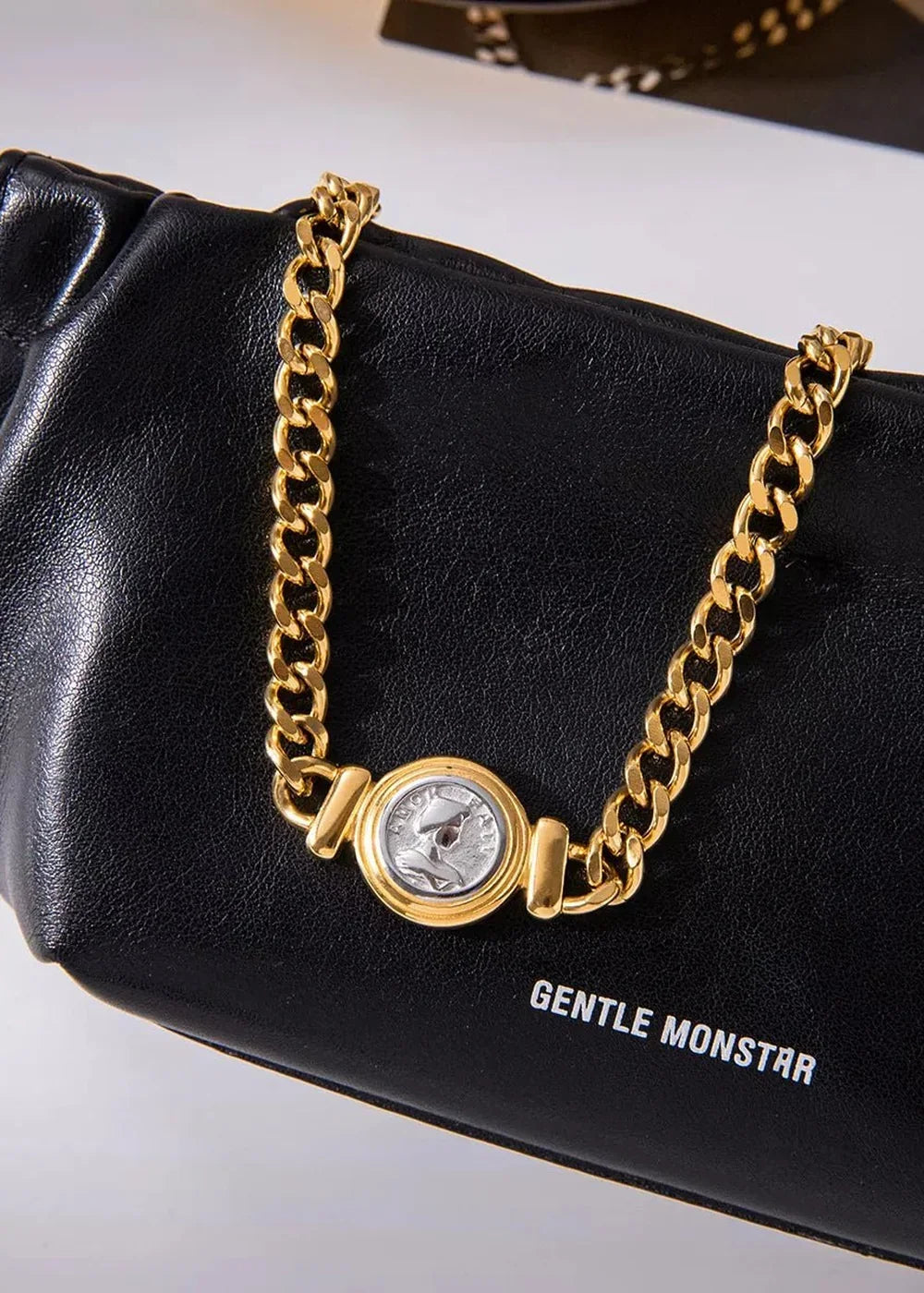 Black leather bag with a gold chain featuring a coin pendant and embossed logo.