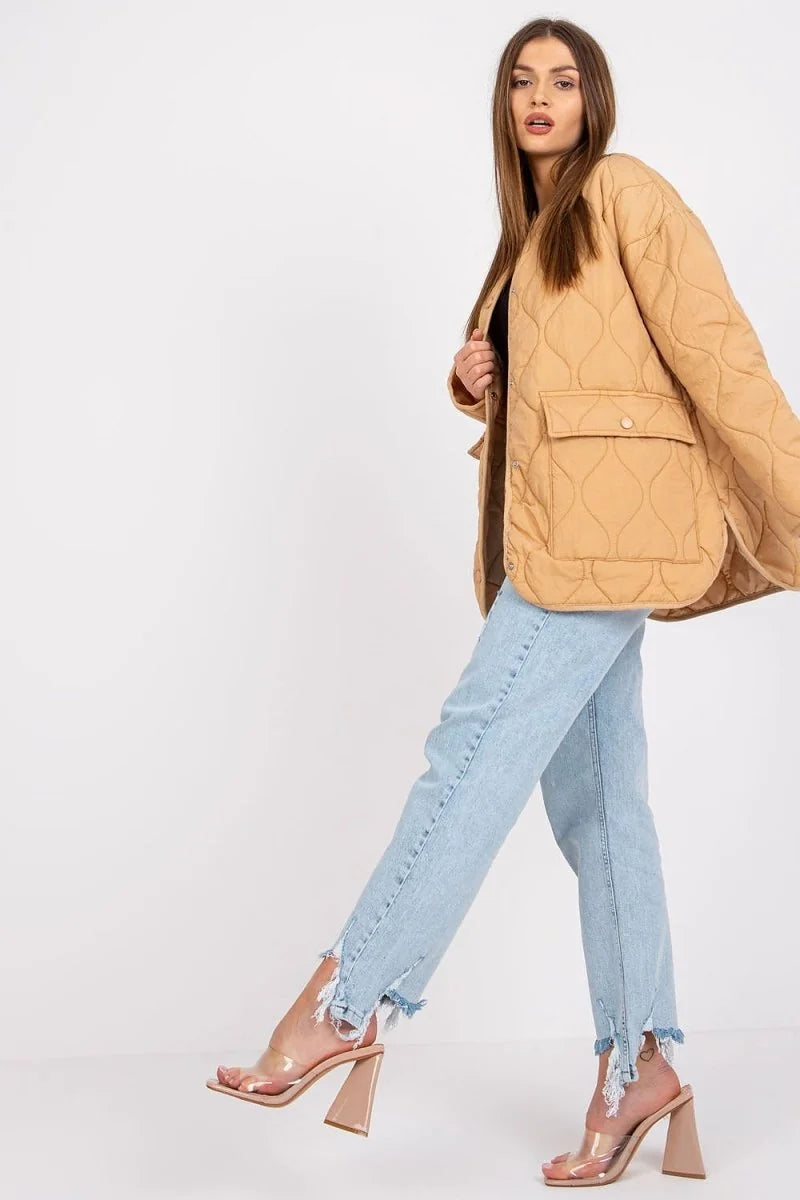 Light brown quilted jacket with pockets, worn by a model with light blue jeans and clear heels.