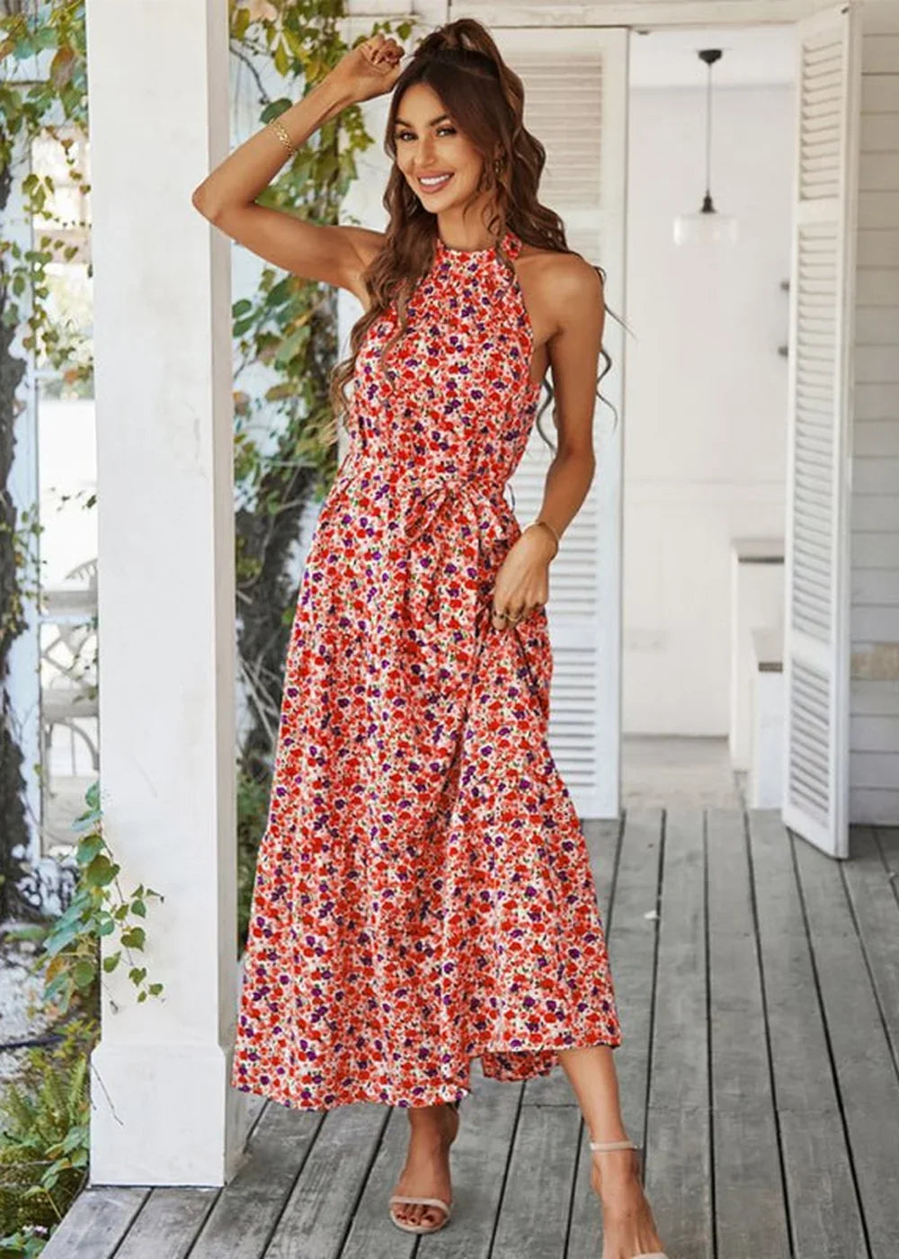 Woman in a red floral print halter maxi dress with a tie waist, standing on a wooden porch.