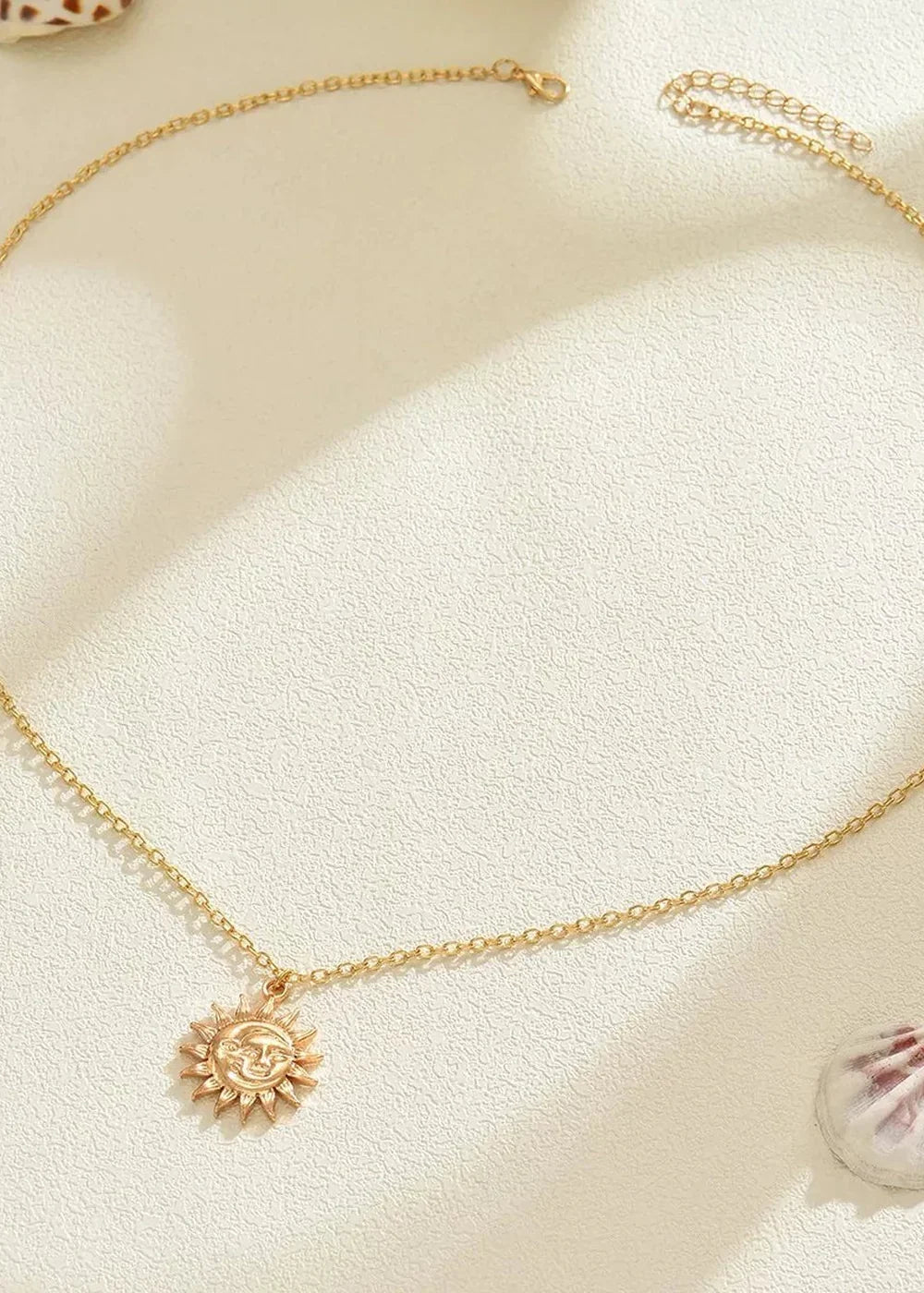 Gold-toned necklace with a sun pendant, featuring a textured face and sun rays, against a light textured background.