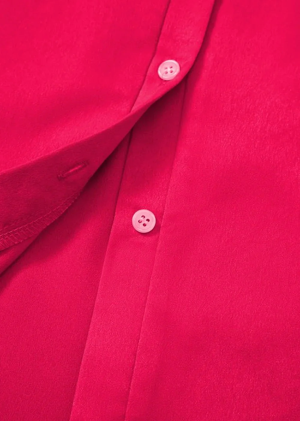 Close-up of a bright pink polyester shirt showing two white buttons and seams.