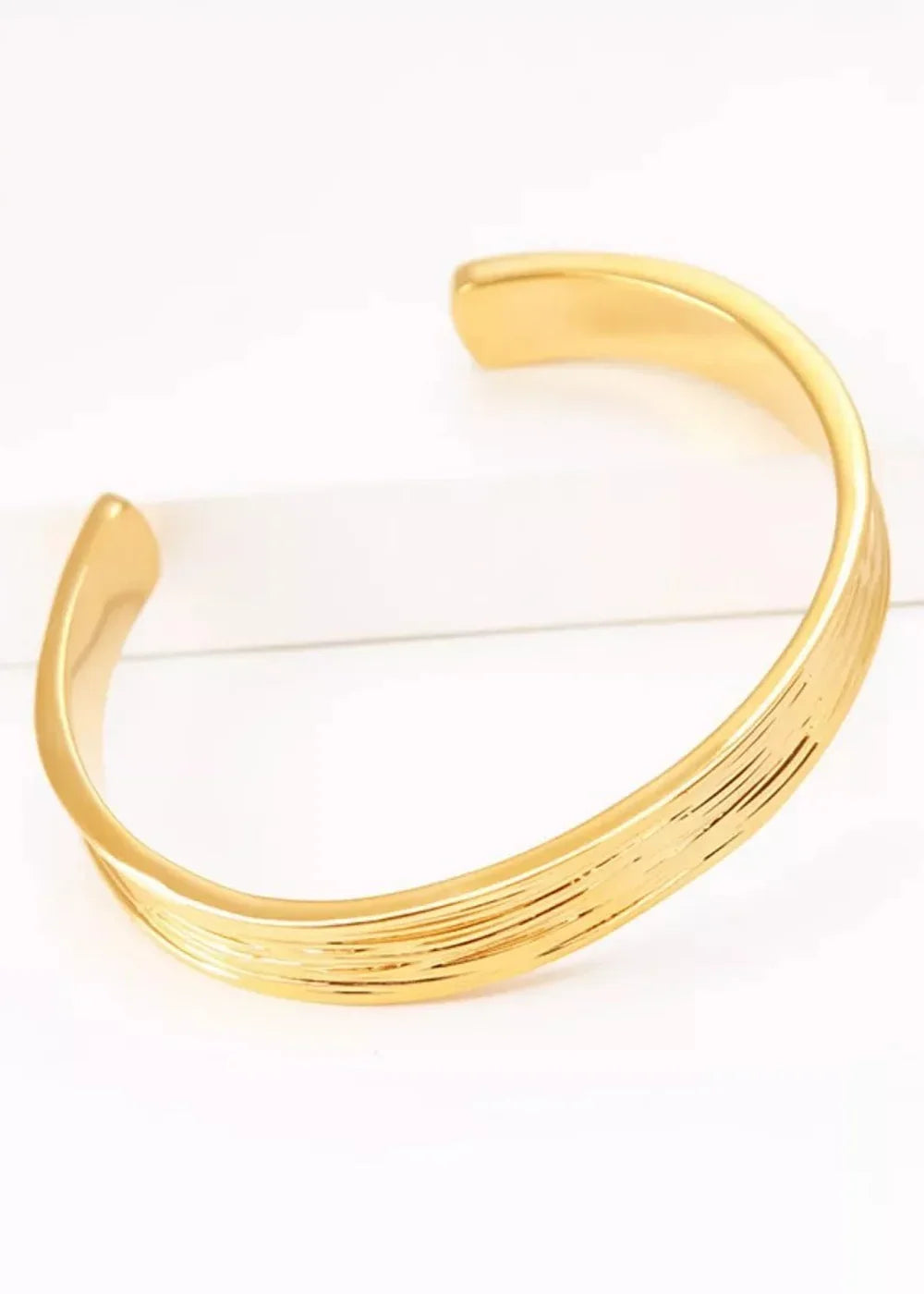 Gold cuff bracelet with textured, wavy lines and an open design.
