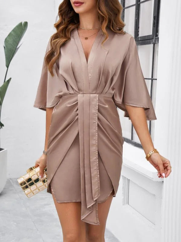 Satin taupe mini dress with a draped bodice, V-neck, and tie waist, worn by a model with a gold clutch.