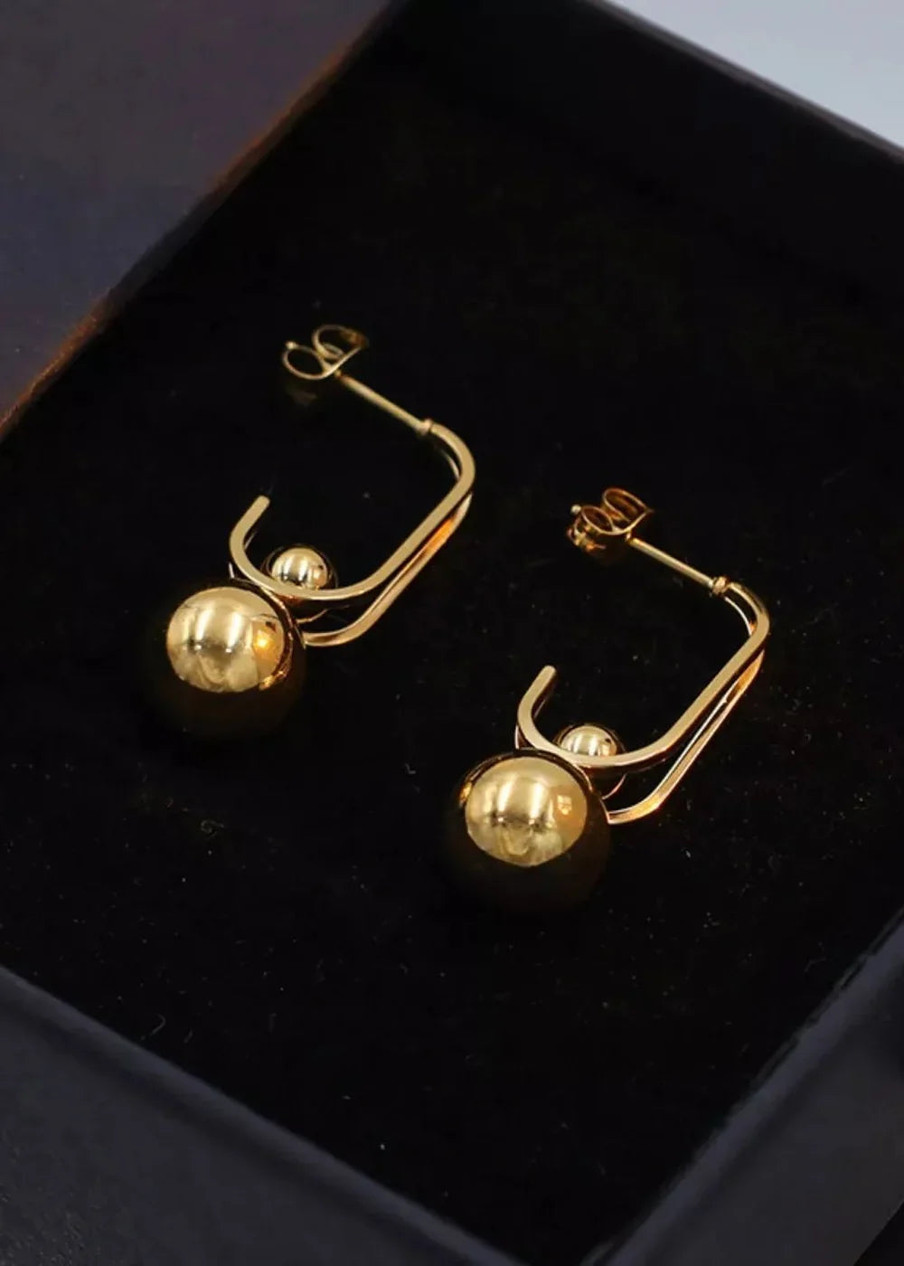 Gold-toned hoop earrings with a dangling sphere and a smaller bead accent.
