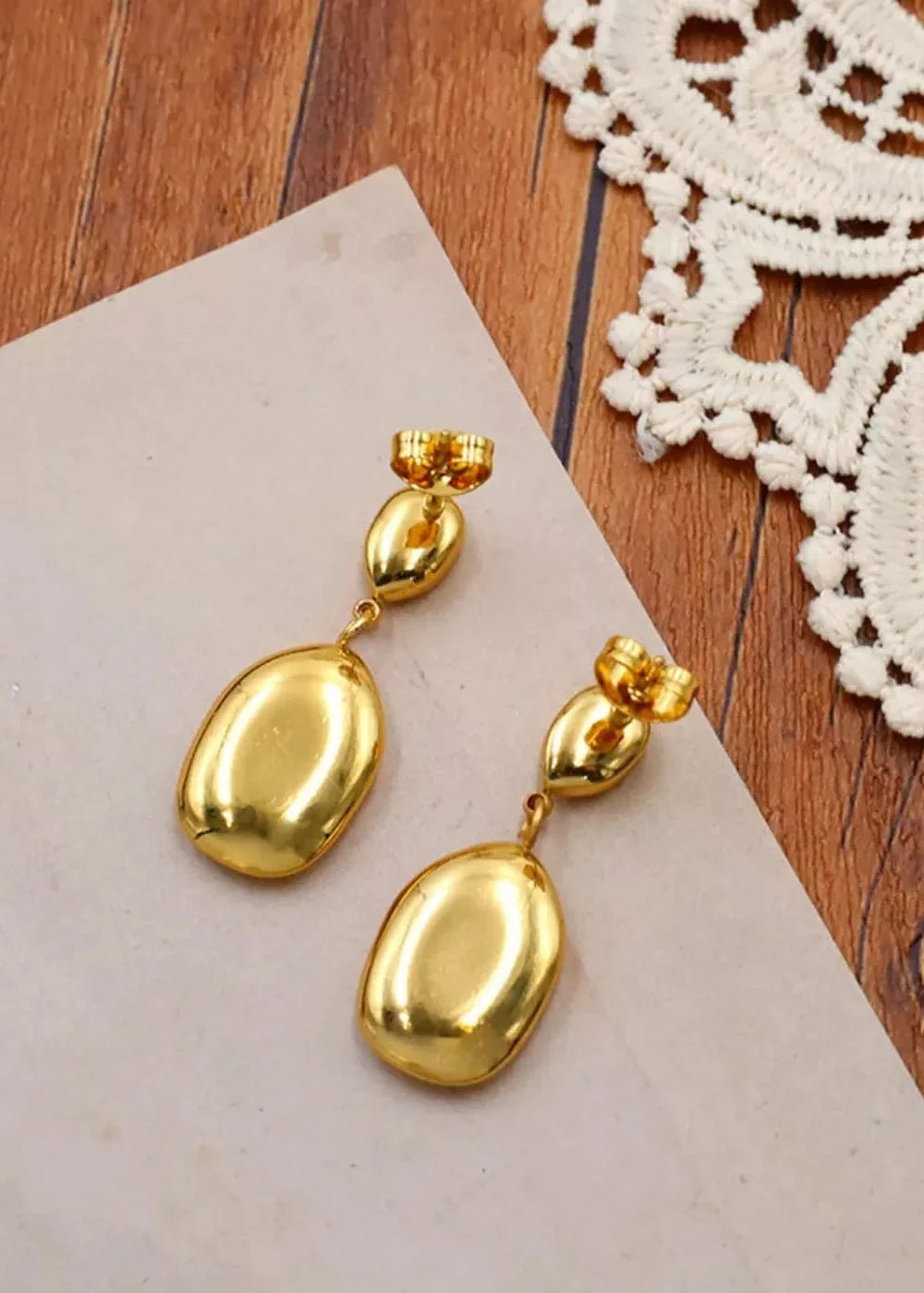 Gold drop earrings with oval pendants, featuring a polished finish on a textured surface.