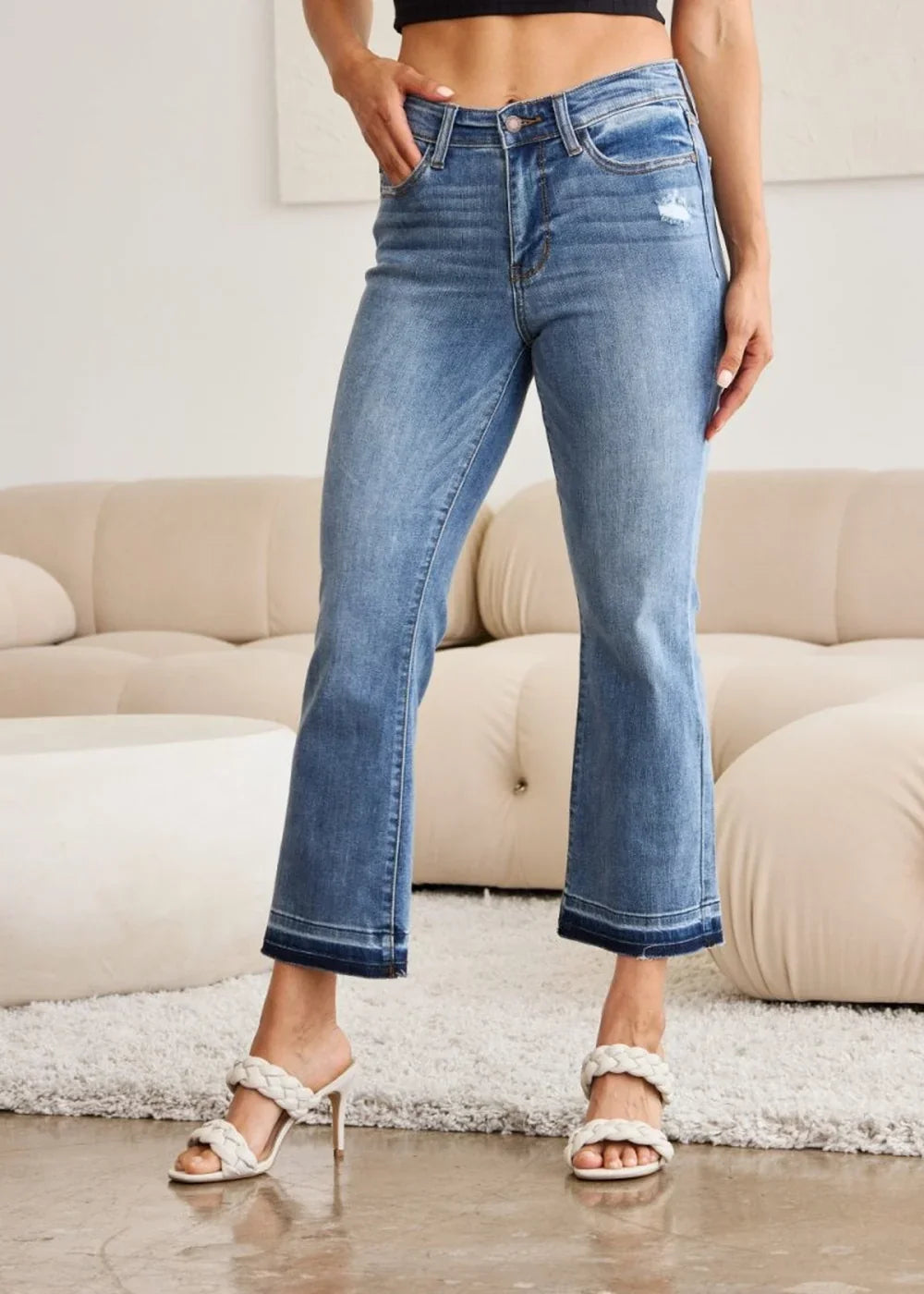 Light wash denim jeans with a distressed detail, frayed hem, and flared leg, worn by a model with white braided heels.