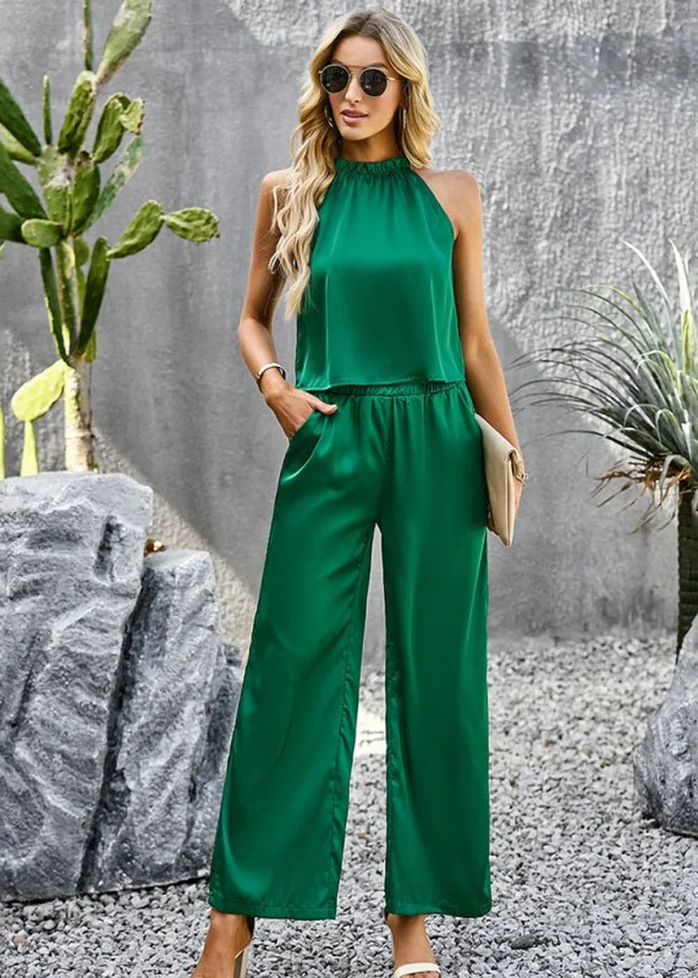 Woman in a green satin halter top and wide-leg pants, holding a clutch.