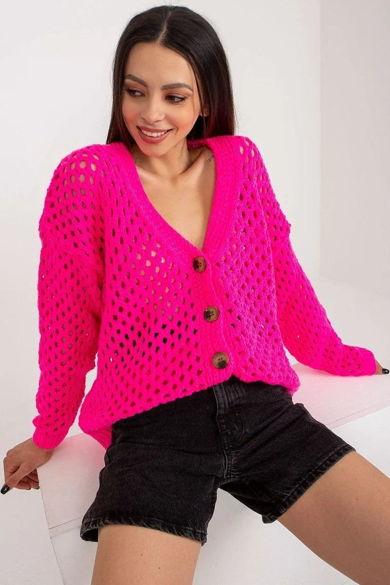 Cropped neon pink crochet cardigan with brown buttons and short black denim shorts on a model.