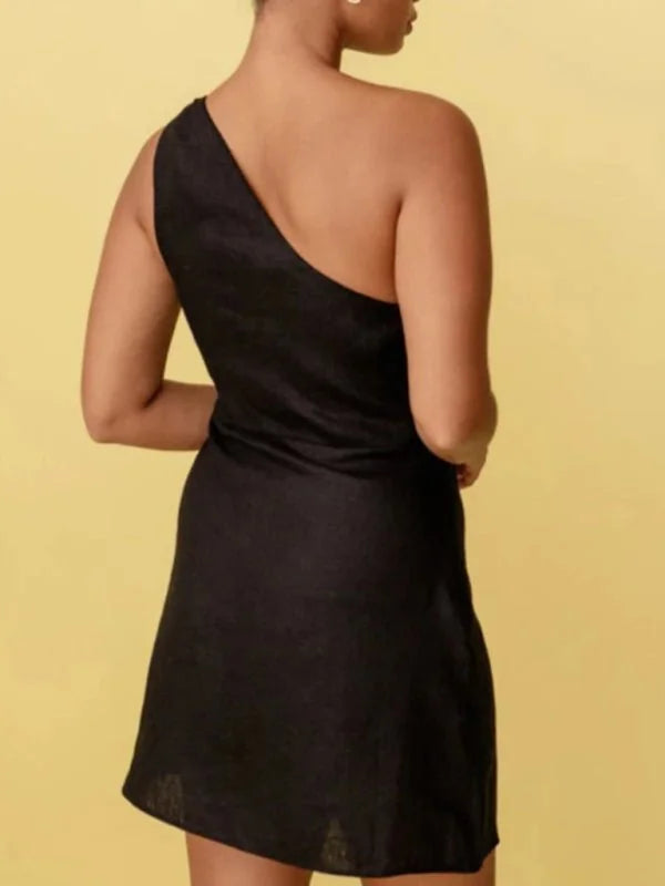 Back view of a black one-shoulder mini dress with a slight sheen, shown on a model against a yellow background.